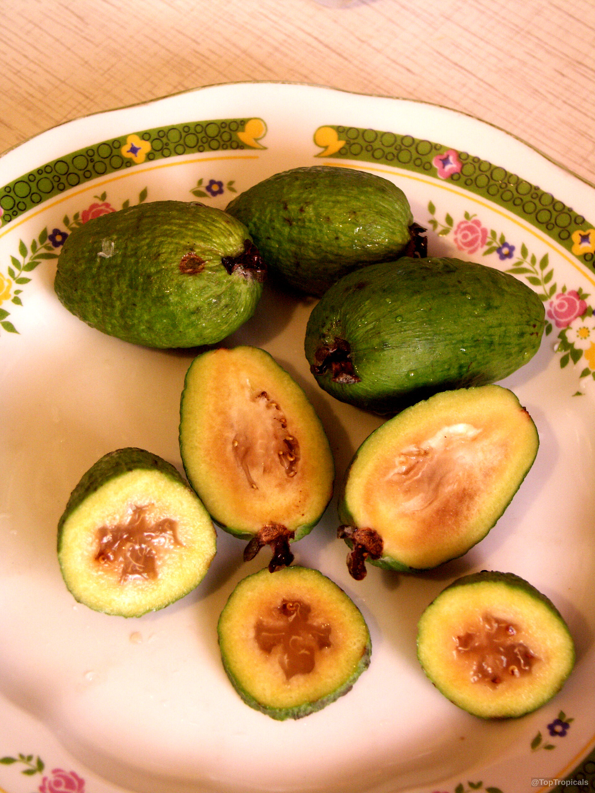 Feijoa sellowiana (Feijoa) whole and sliced oval green fruit rests on a plate. Feijoa sellowiana (Feijoa) green fruit, sliced on a plate, close up.
