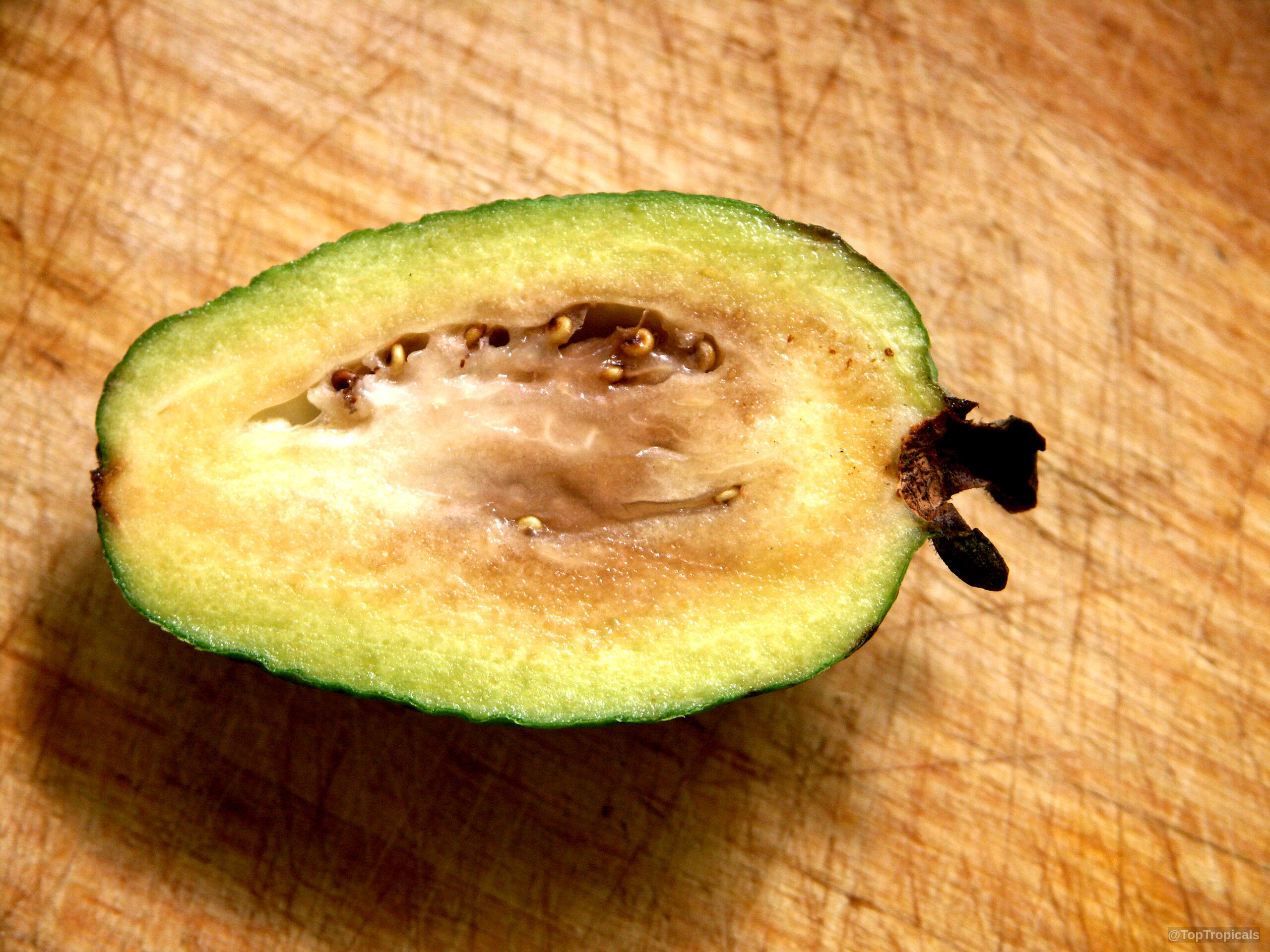 Feijoa sellowiana (Feijoa) halved fruit revealing creamy center with tiny seeds on a surface. Feijoa sellowiana (Feijoa) sliced green fruit close up with tiny seeds on a surface.